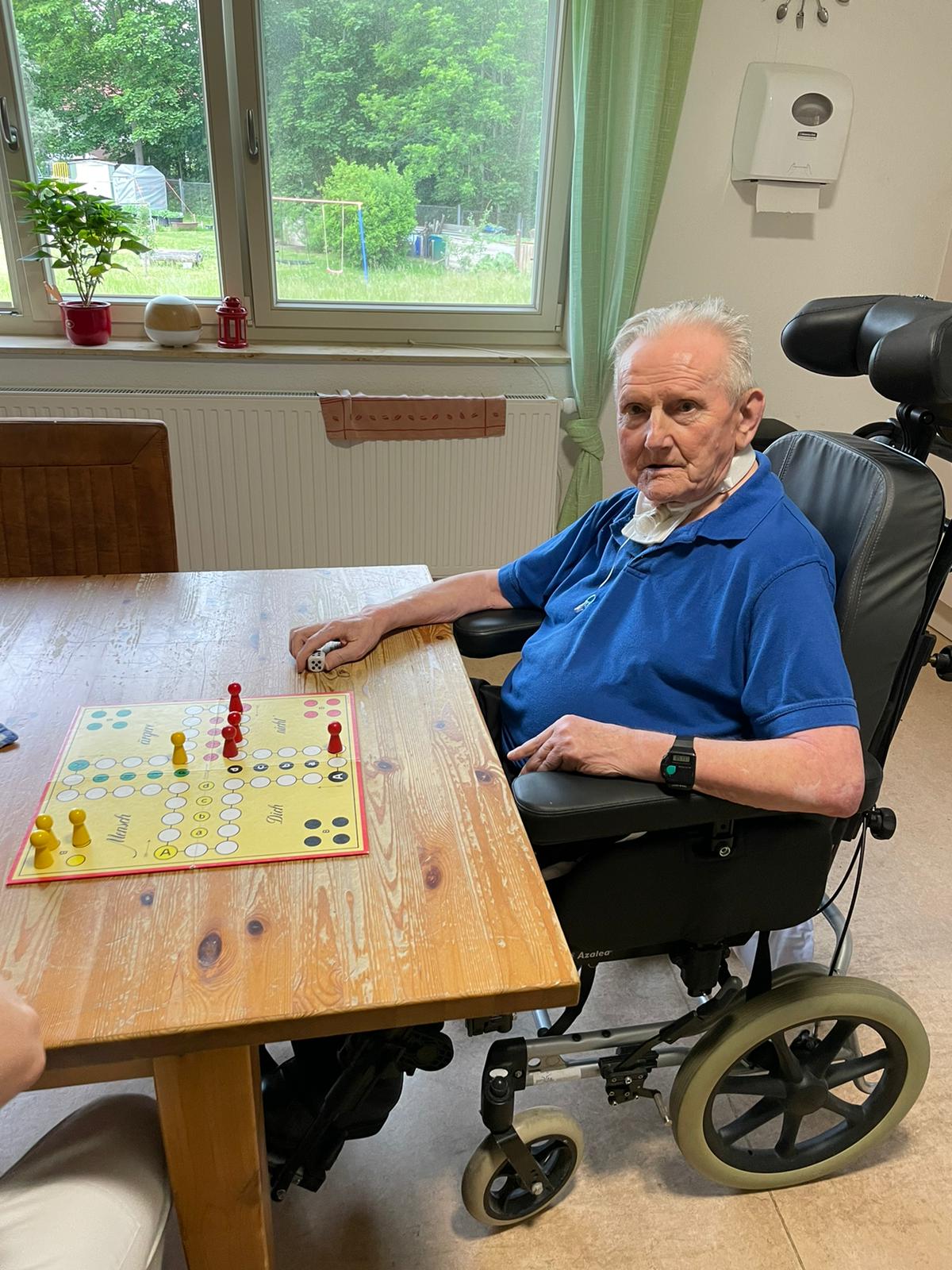 Älterer Mann im Rollstuhl beim Gesellschaftsspiel ‚Mensch ärgere dich nicht‘.